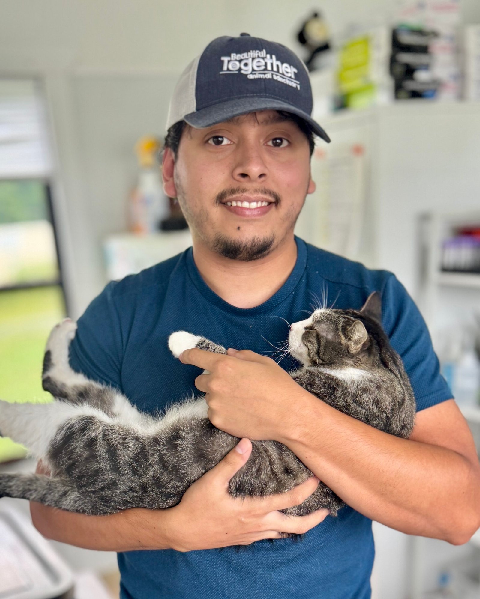 young man with a beautiful together animal sanctuary ball cap holding a beautiful tabby and white cat